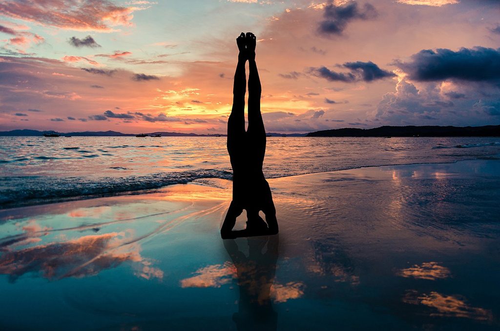 Ocean sunset with Male doing head stand Yoga pose